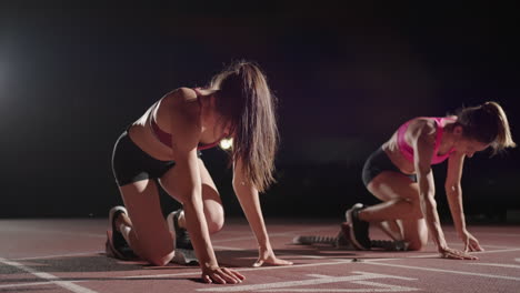 A-row-of-runners-womens-crouch-in-the-starting-position-before-beginning-to-race.-Females-start-with-running-shoes-on-the-stadium-from-the-start-line-in-the-dark-with-spotlights-in-slow-motion.